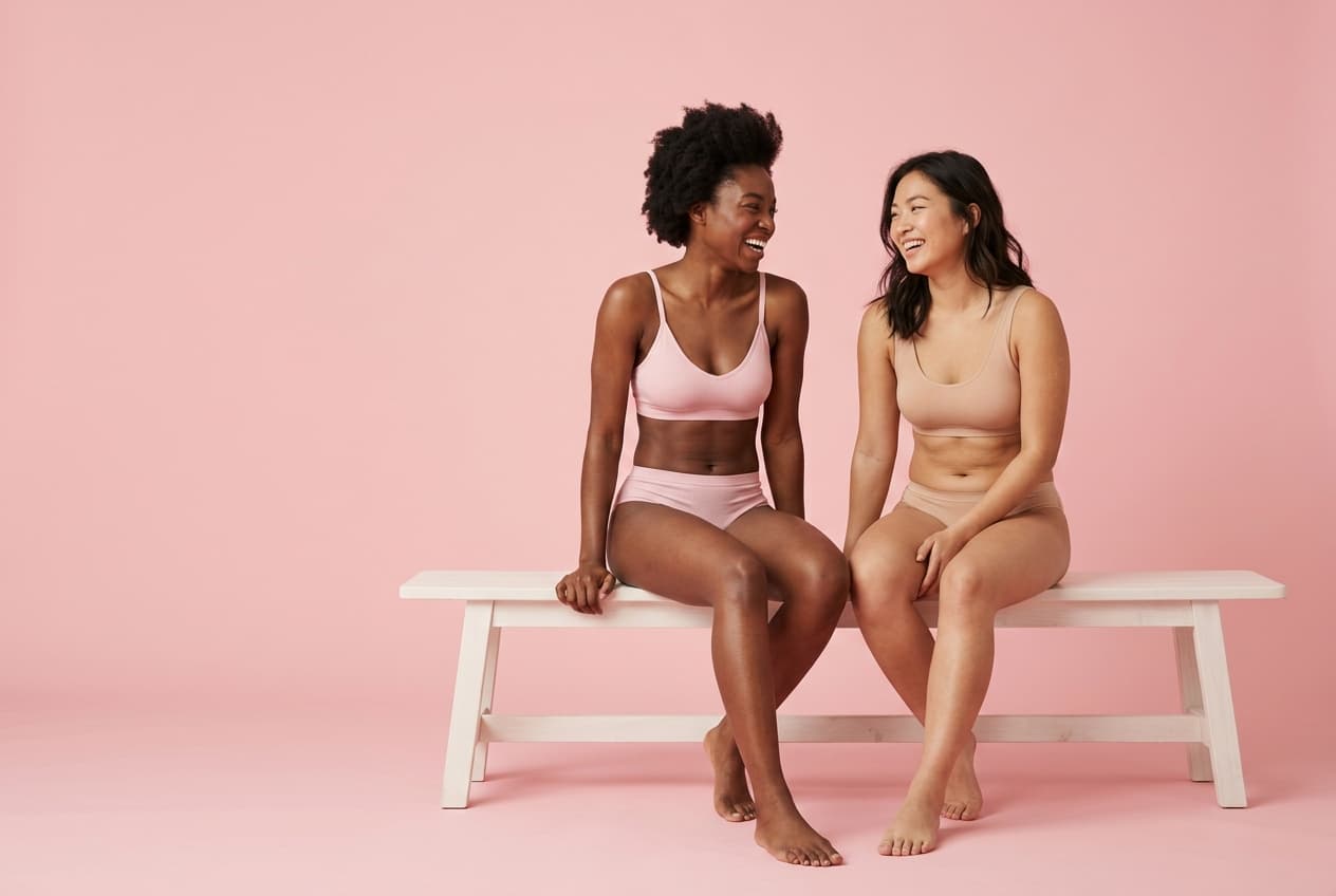 Two women laughing on a bed wearing LIVRA underwear